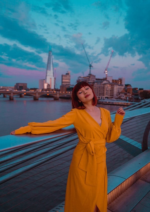 A woman in a Sarvin Mustard Wrap Dress posing on a bridge in London.