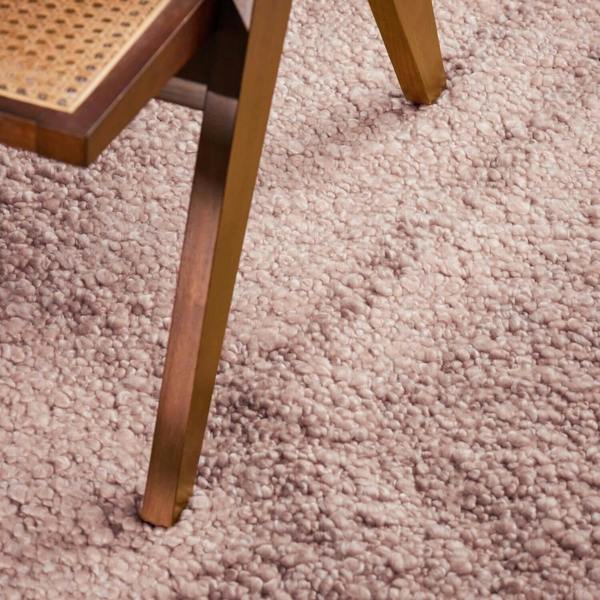 Close-up of a wooden chair leg on a textured pink carpet