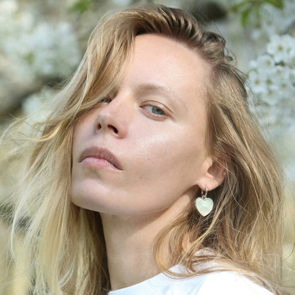 Silver heart charm earrings by LENAE London worn by a fashion model with blossom behind.