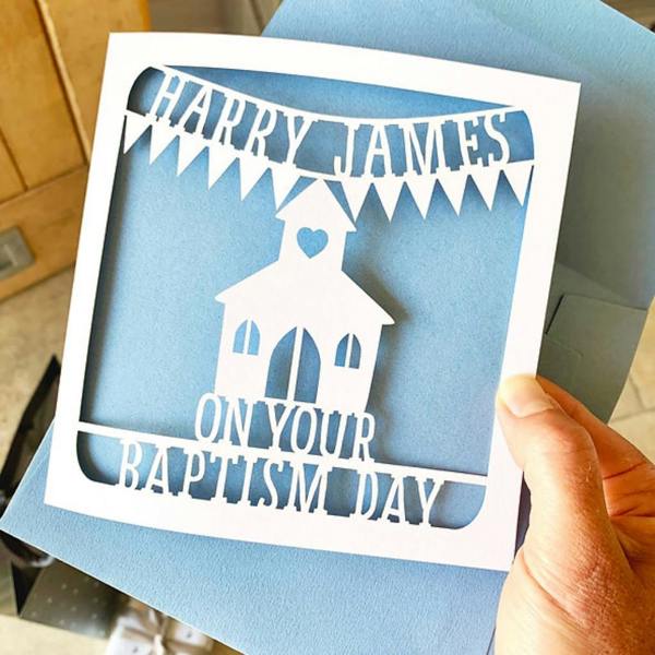 Personalised papercut baptism card with the name Harry James on bunting above a church against a light blue paper insert