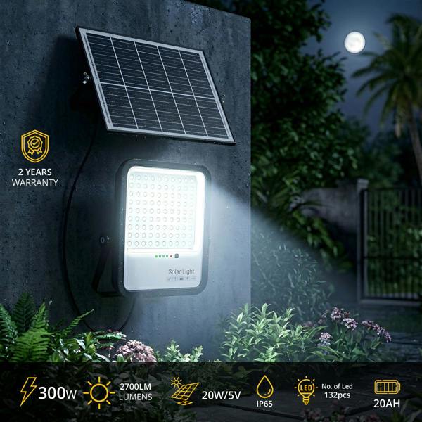 Solar light fixture with solar panel on a wall at night, surrounded by plants.