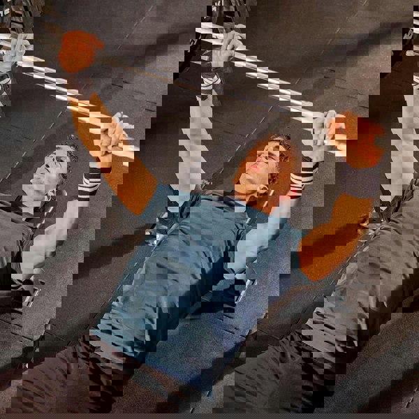 Man performing a bench press with a barbell in a gym setting wearing  adidas wrist wraps