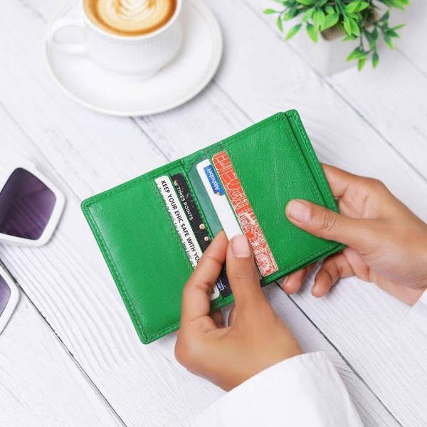 Green wallet with cards held by hands on a white surface with a cup of coffee and plant in the background