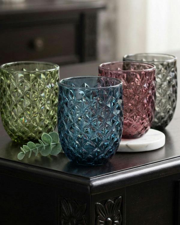 Four textured glass tumblers on a dark surface with a blurred background