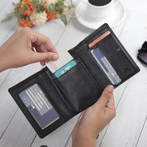 Black wallet with cards held open by a hand on a light wooden surface.