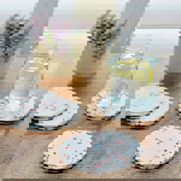 Four round confetti coasters made of recycled plastic on a wooden table.