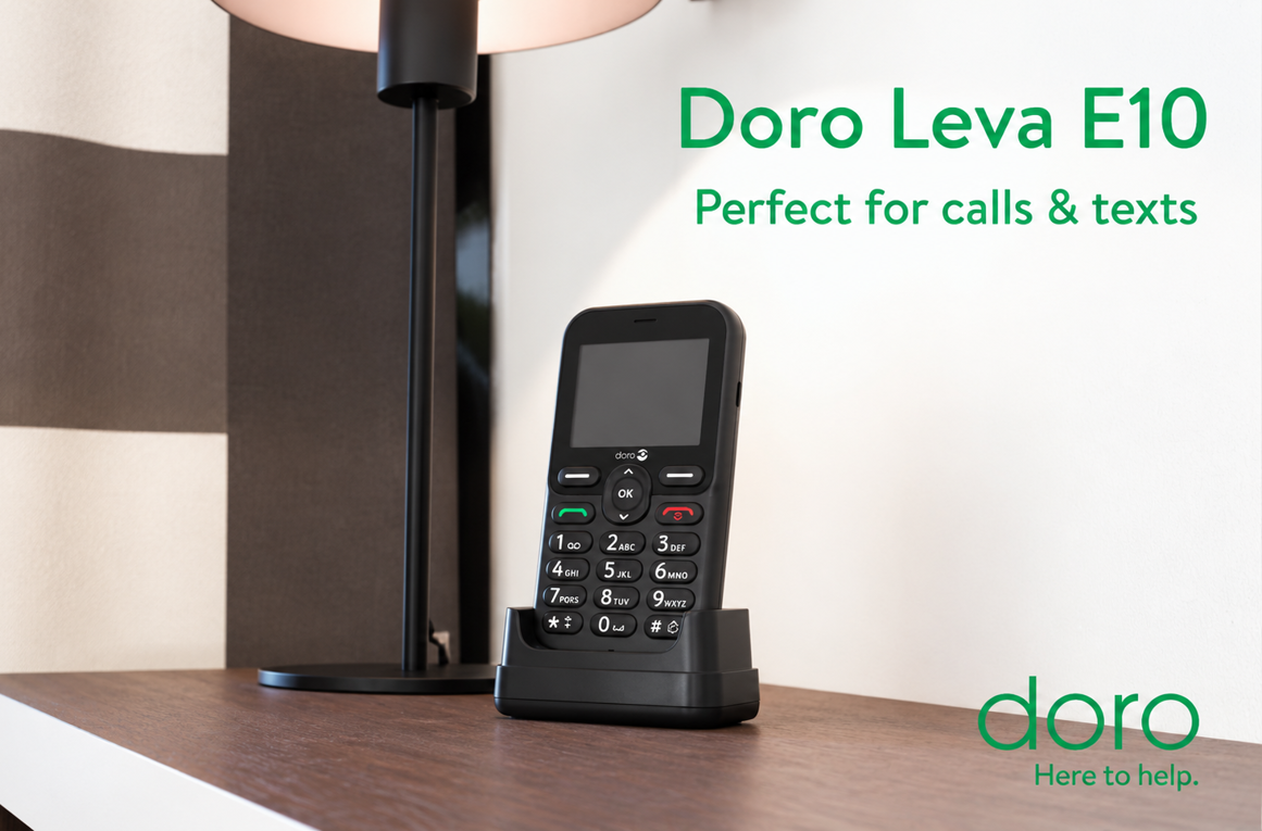 A feature phone device, in a cradle, stood on a table with a lamp behind it. 